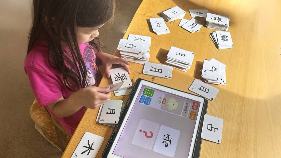 Child playing with Chinese character flash cards next to a tablet, from Mama and Baby Learn Mandarin